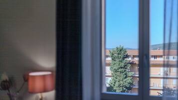Une fenêtre donnant sur un immeuble doté de nombreux balcons, avec un arbre au premier plan.