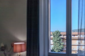 Une fenêtre donnant sur un immeuble doté de nombreux balcons, avec un arbre au premier plan.