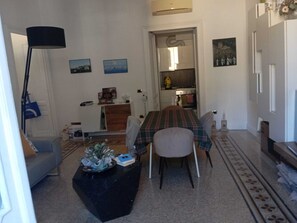 Ein Wohnzimmer mit einer Couch, einem Couchtisch und einem Esstisch für zwei Personen. Durch eine offene Tür ist eine Küche erkennbar.