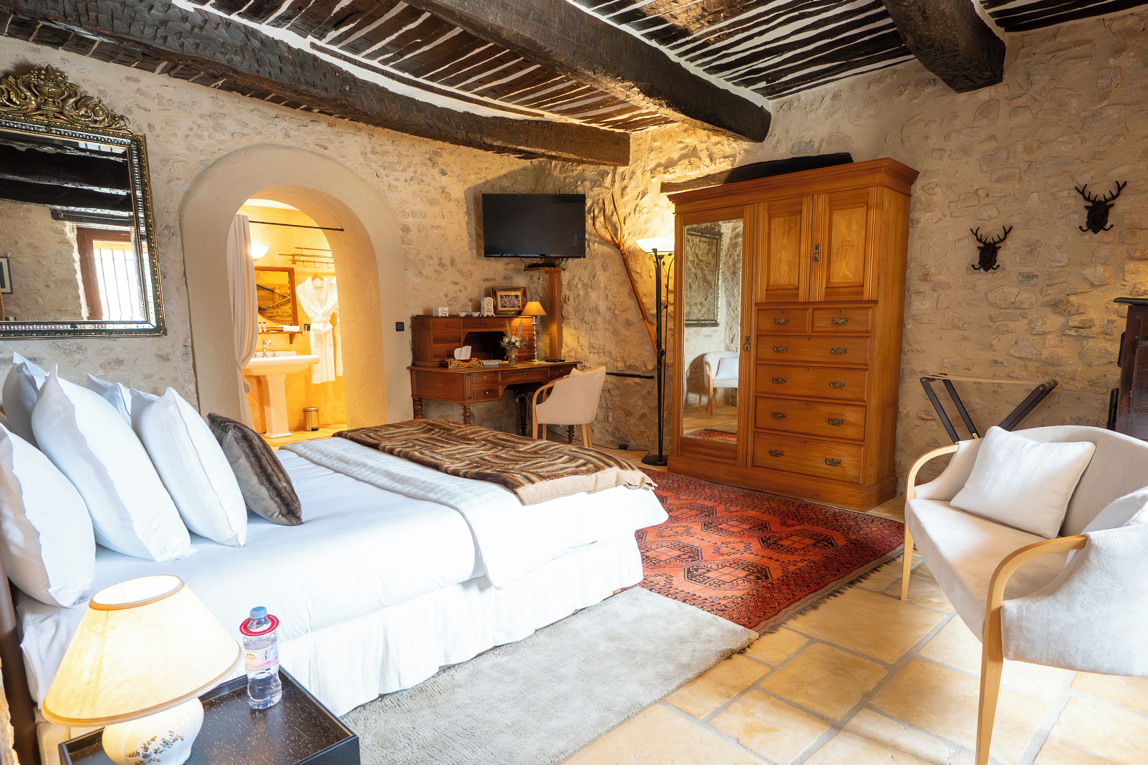 A bedroom with a bed, a dresser, a television, and a stone wall.