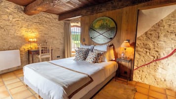 A bedroom with a stone wall, a bed with a white bedspread, a wooden headboard, and a large window with a view.