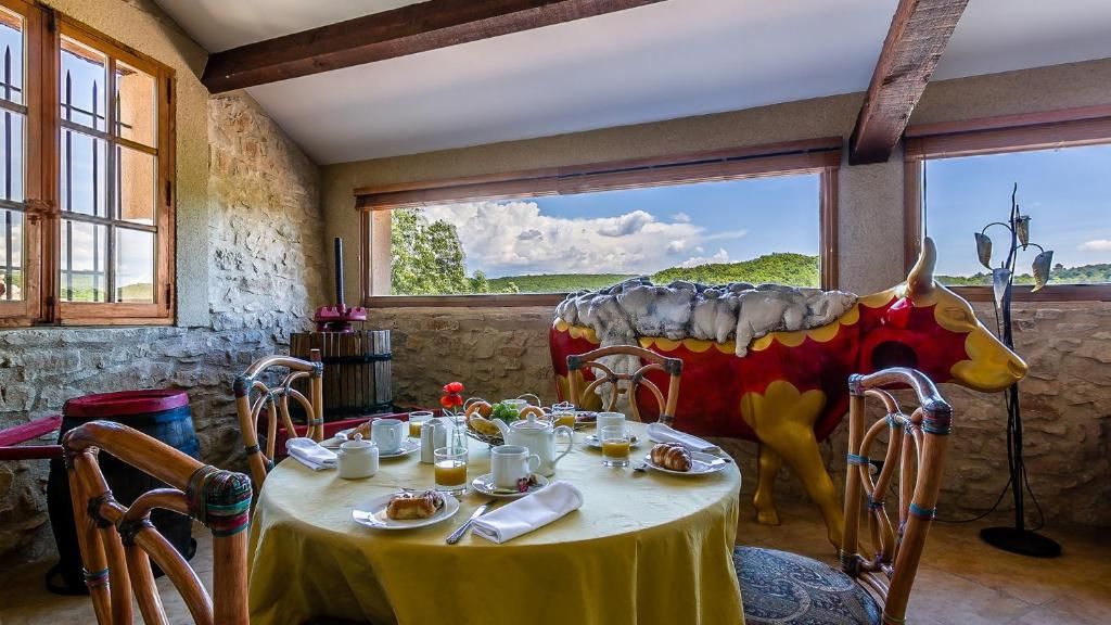 A dining area with a round table set for breakfast, a bull statue, and a view of the countryside.