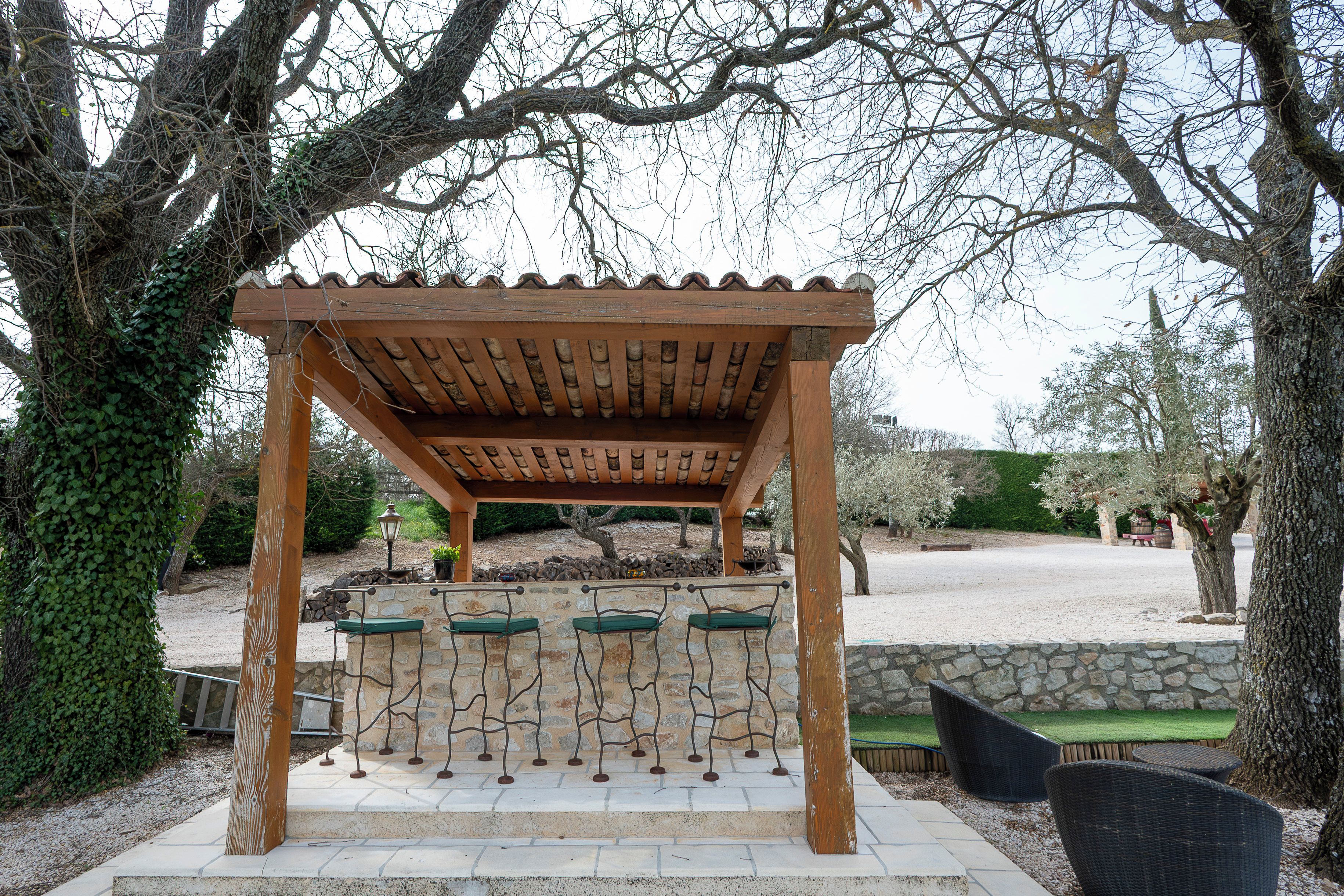 Una pérgola de madera con techo de tejas, paredes de piedra y asientos acolchados de color verde.