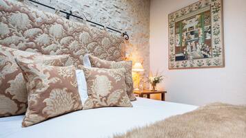 A bedroom with a stone wall, a bed with patterned pillows, a nightstand with a lamp, and a framed picture on the wall.