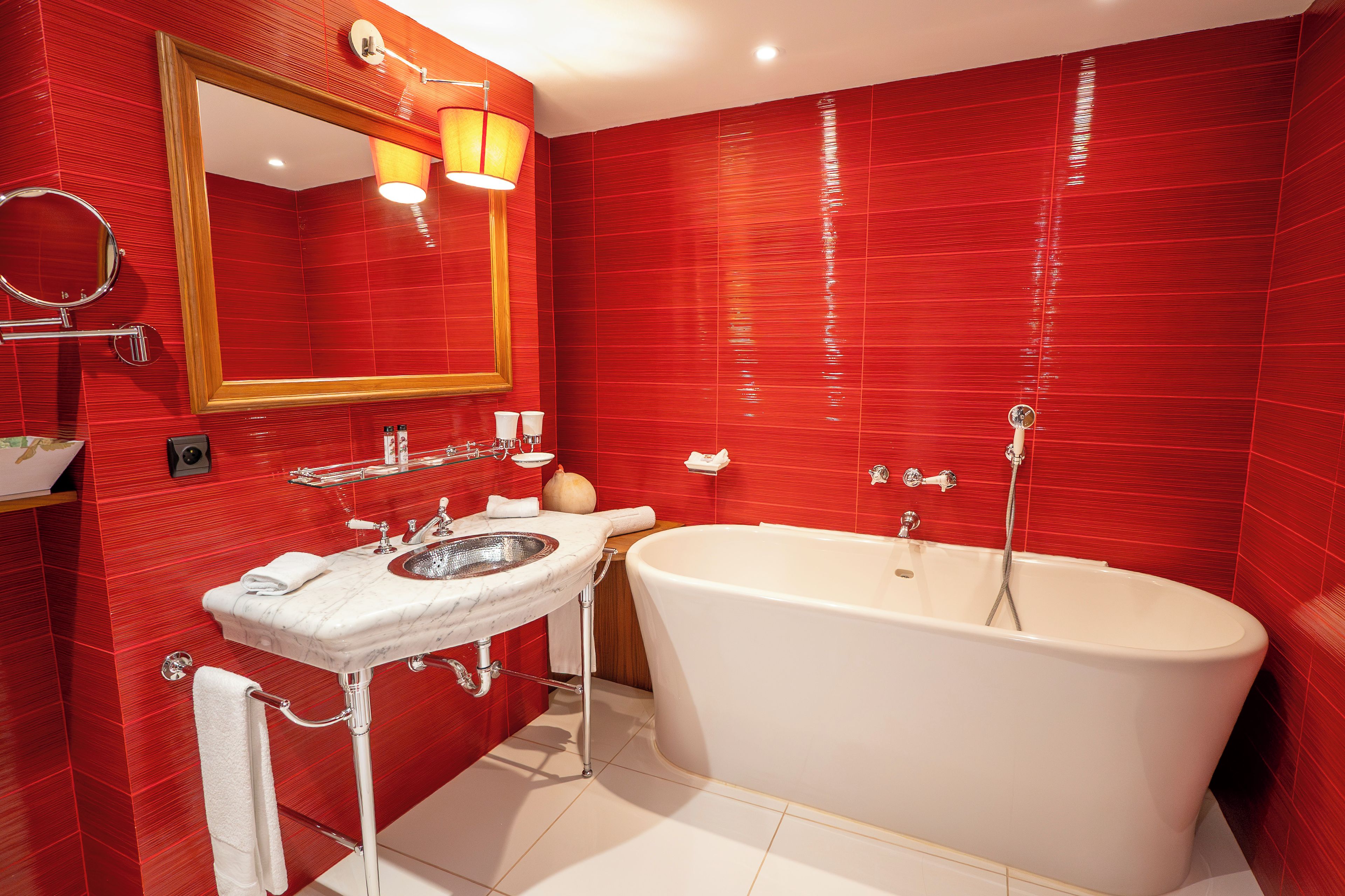 A bathroom with a white bathtub, a sink with a mirror, and red tiled walls.