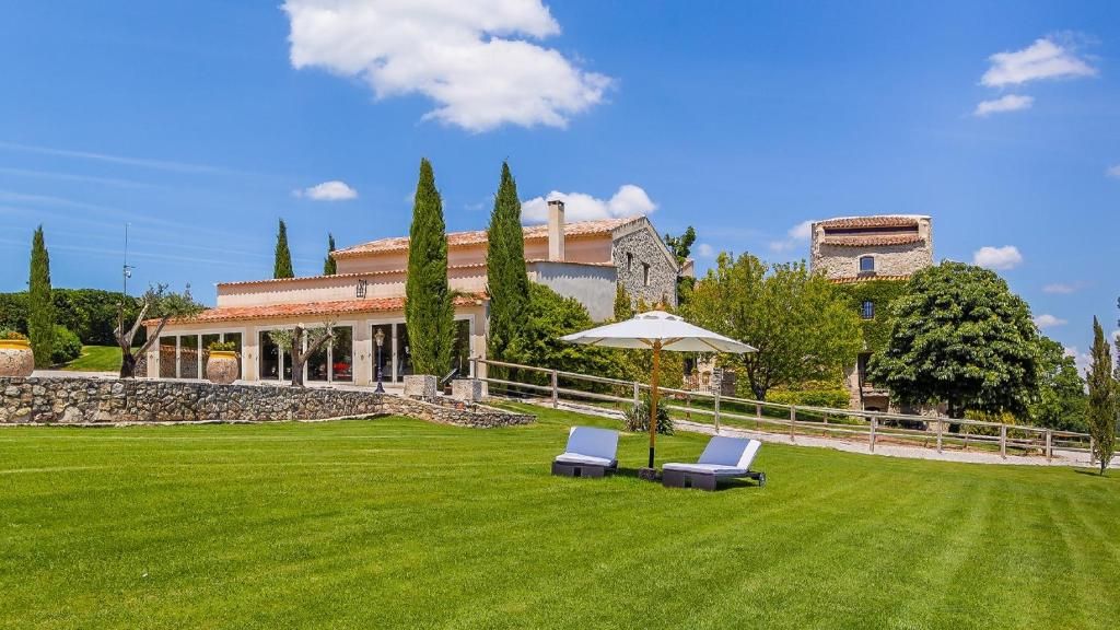 Eine Villa mit Mauerwerk, einer überdachten Terrasse und einem Rasen mit Liegestühlen.