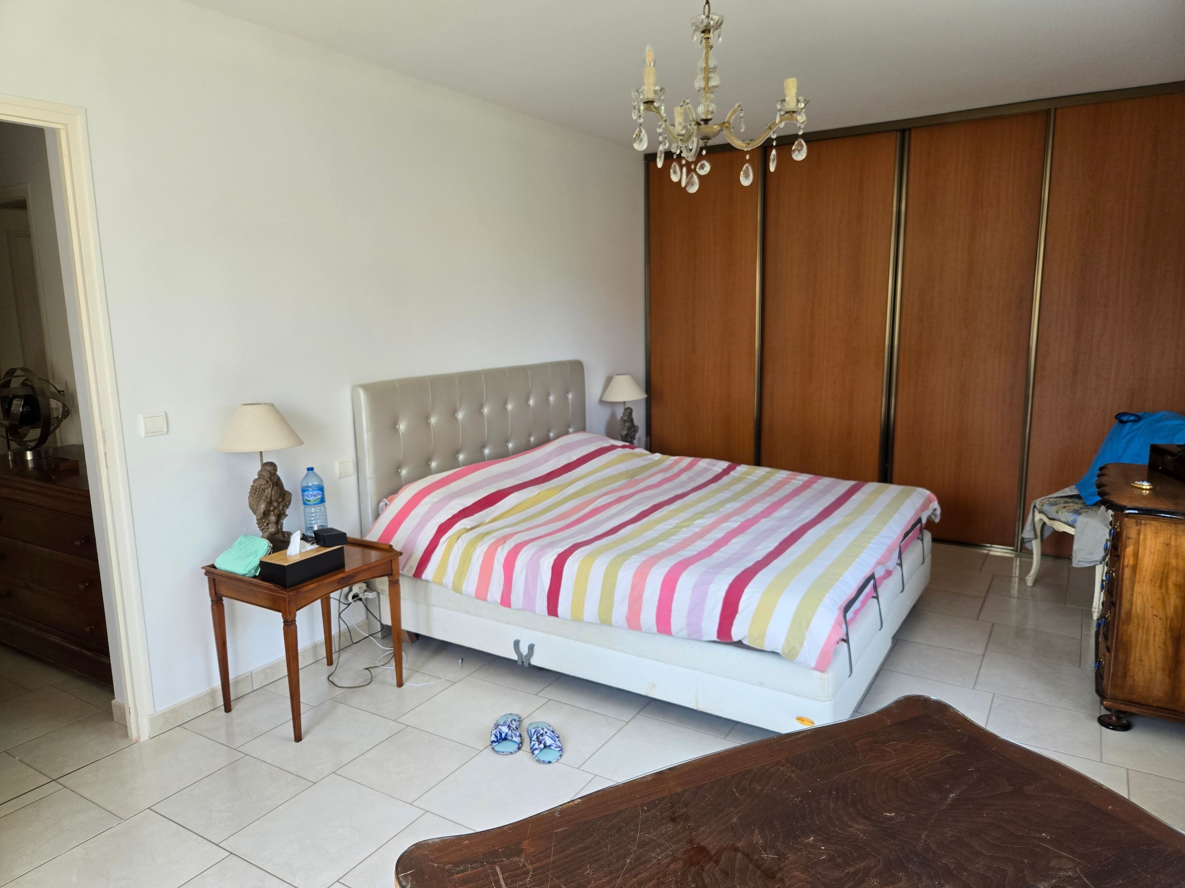 Een slaapkamer met een bed, nachtkastje, lamp en een houten garderobe.