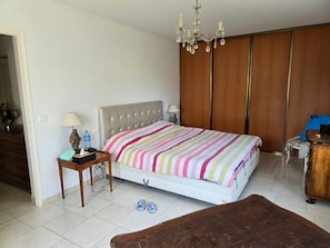 Een slaapkamer met een bed, nachtkastje, lamp en een houten garderobe.