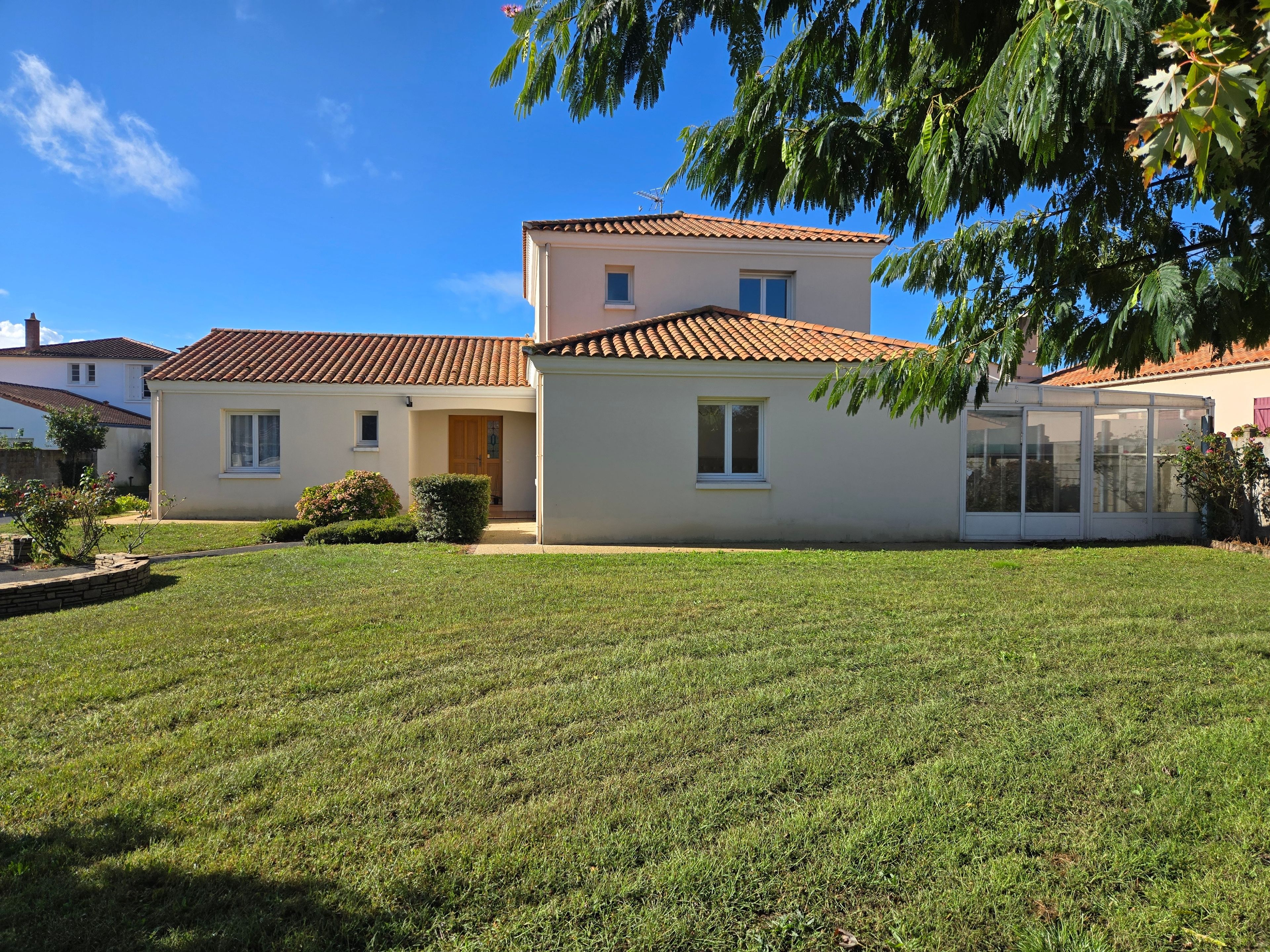 A two-story house with a tiled roof, a covered patio, and a well-maintained lawn.