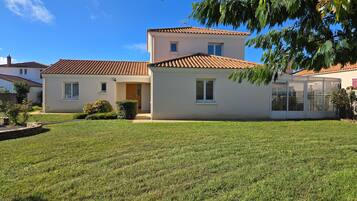A two-story house with a tiled roof, a covered patio, and a well-maintained lawn.