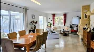 Een moderne woonkamer met een eethoek, witte banken, een salontafel en een televisie.