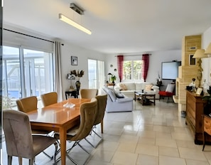Een moderne woonkamer met een eethoek, witte banken, een salontafel en een televisie.