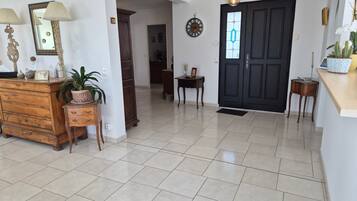 A spacious room with a tiled floor, a wooden dresser, a mirror, a door with a decorative glass panel, and a hanging light fixture.