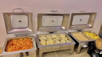 A buffet with various food items including a dish with vegetables, a tray of white cubes, and a container of yellow fruit.