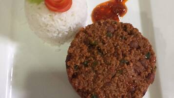 Un plato con arroz blanco cubierto con una rodaja de tomate, una hamburguesa y un poco de salsa.
