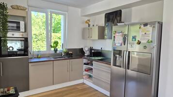 A modern kitchen with stainless steel appliances, wooden flooring, and a window with a view of greenery.