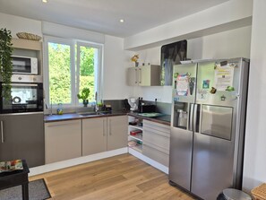 A modern kitchen with stainless steel appliances, wooden flooring, and a window with a view of greenery.
