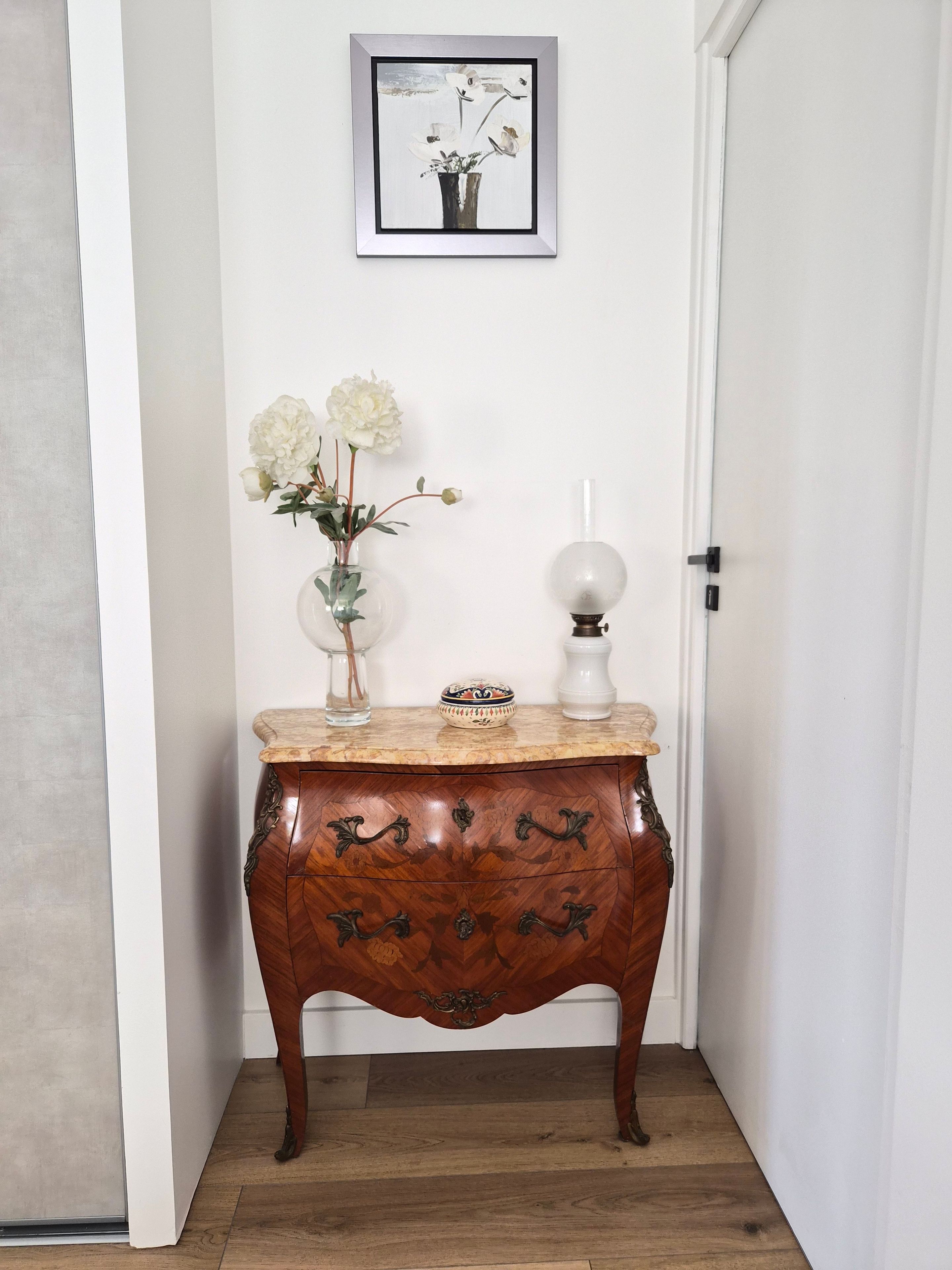 Una mesita de madera con un florero y una lámpara frente a una pared blanca.