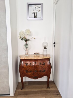 A wooden side table with a vase of flowers and a lamp against a white wall.