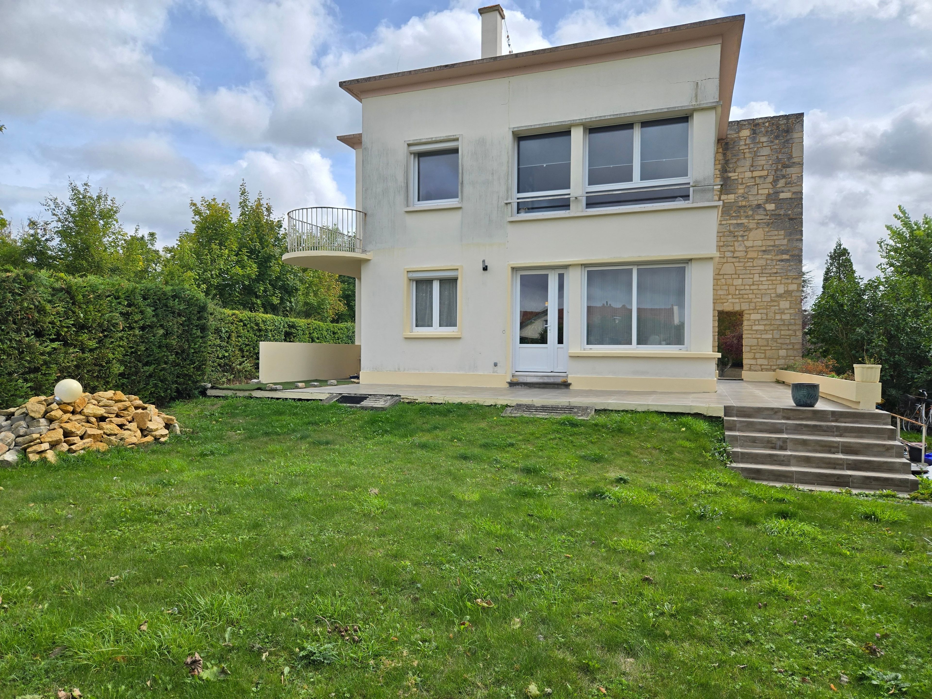 Ein zweistöckiges Haus mit einer Stein-Fassade, einem Balkon und einem gepflegten Rasen.