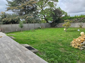 A backyard with a grassy lawn, a stone wall, and a wooden deck.