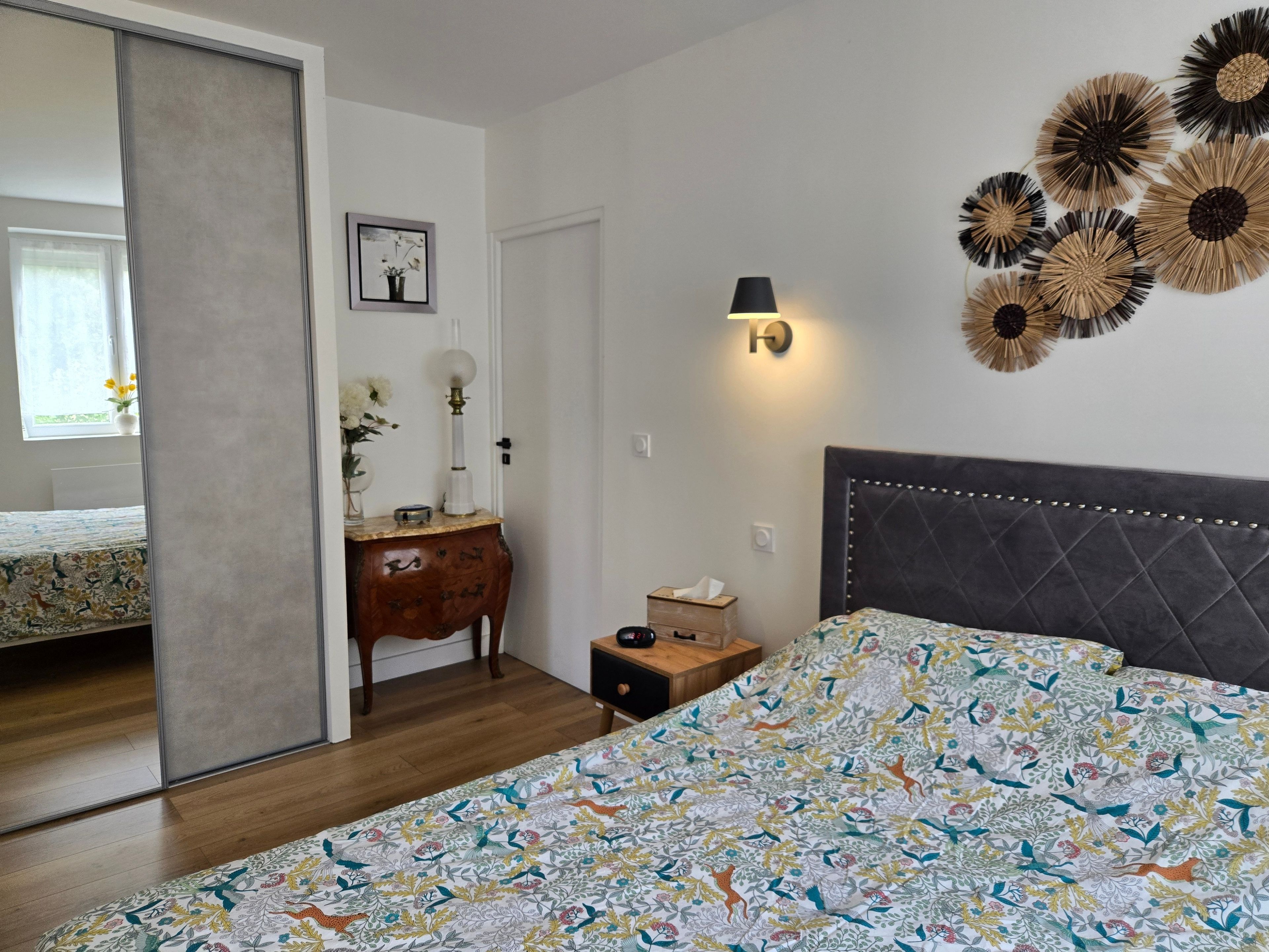Ein Schlafzimmer mit einem Bett, einem Nachttisch, einer Lampe, einem Spiegel und einer Wanddekoration.