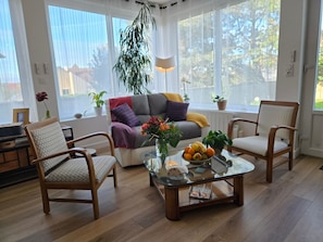 A well-lit living room with a sofa, two armchairs, a coffee table with fruit, and a hanging plant.