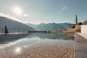 Une piscine à débordement offrant une vue imprenable sur une chaîne de montagnes et un plan d’eau.