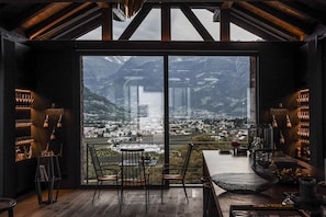 Un intérieur moderne avec une grande fenêtre donnant sur les montagnes, un coin bar avec des verres à vin et un espace salon aménagé.