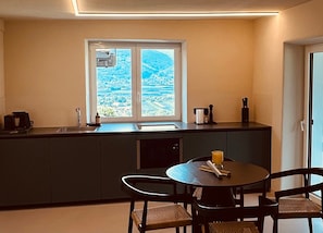 Une cuisine compacte avec une fenêtre donnant sur un paysage, une petite table à manger avec des chaises et les équipements de base.