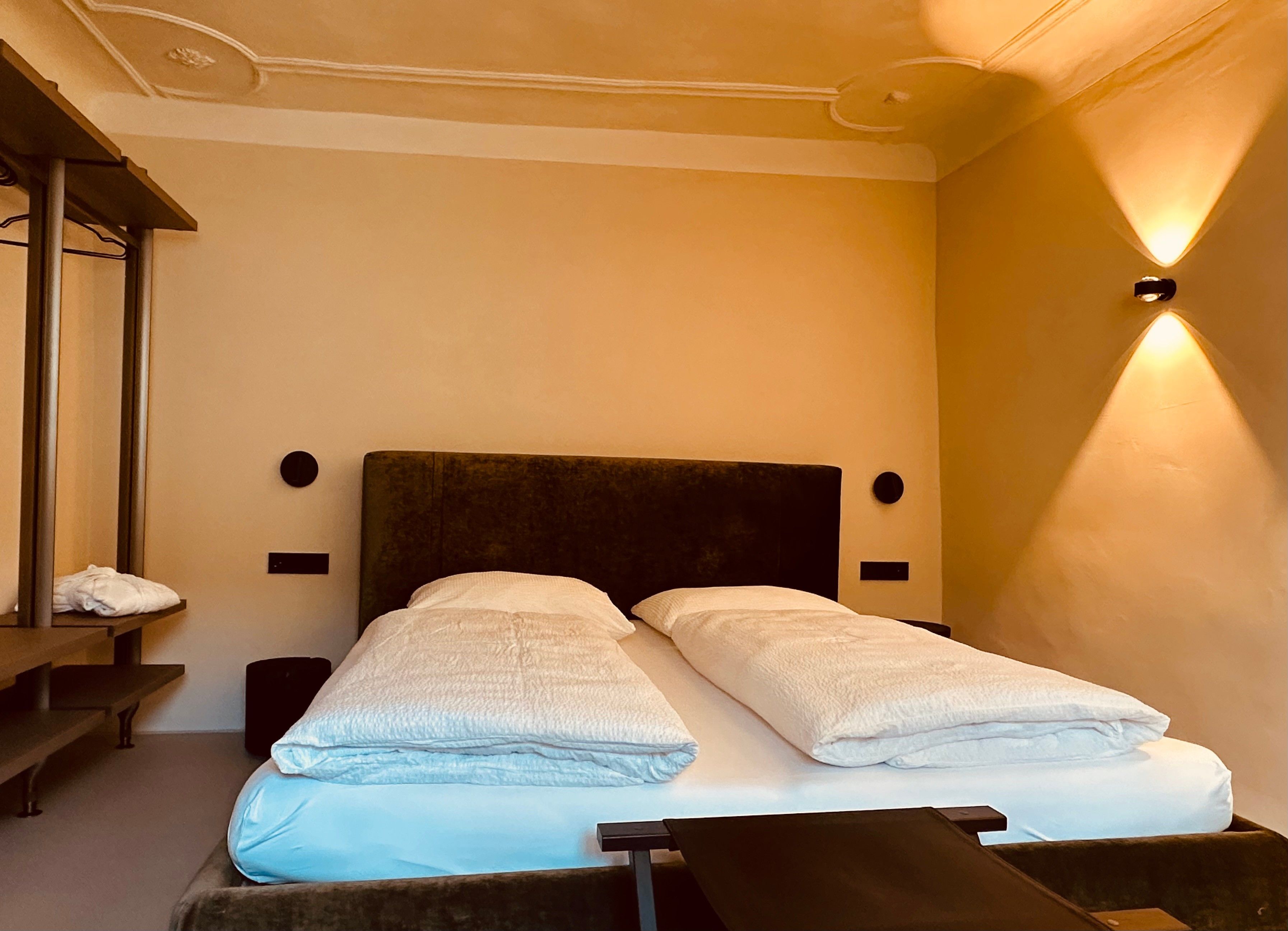 Une chambre d’hôtel avec un lit, un banc et un luminaire fixé au mur.