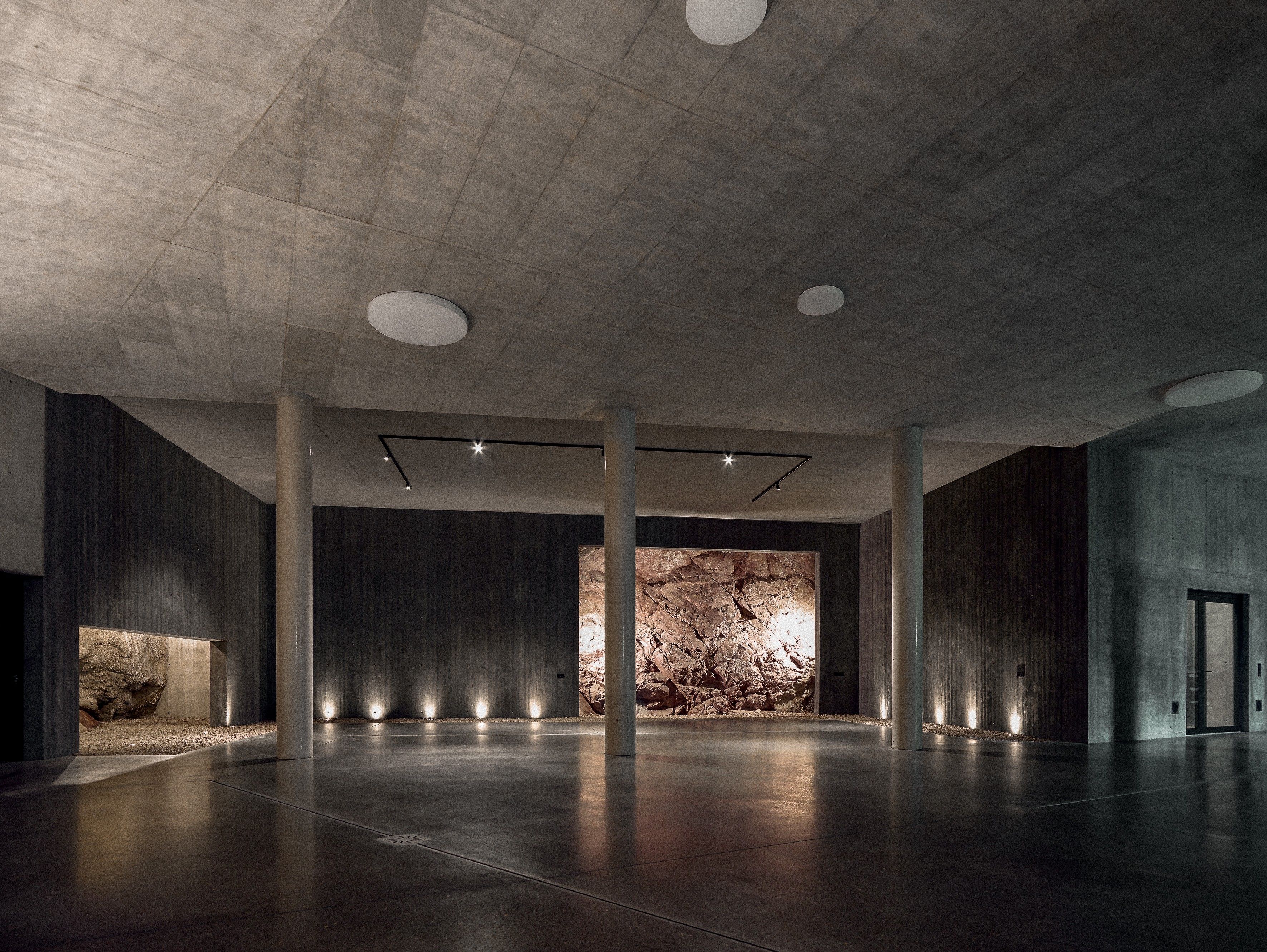 A spacious interior with a high ceiling, concrete walls, and a central rock feature.
