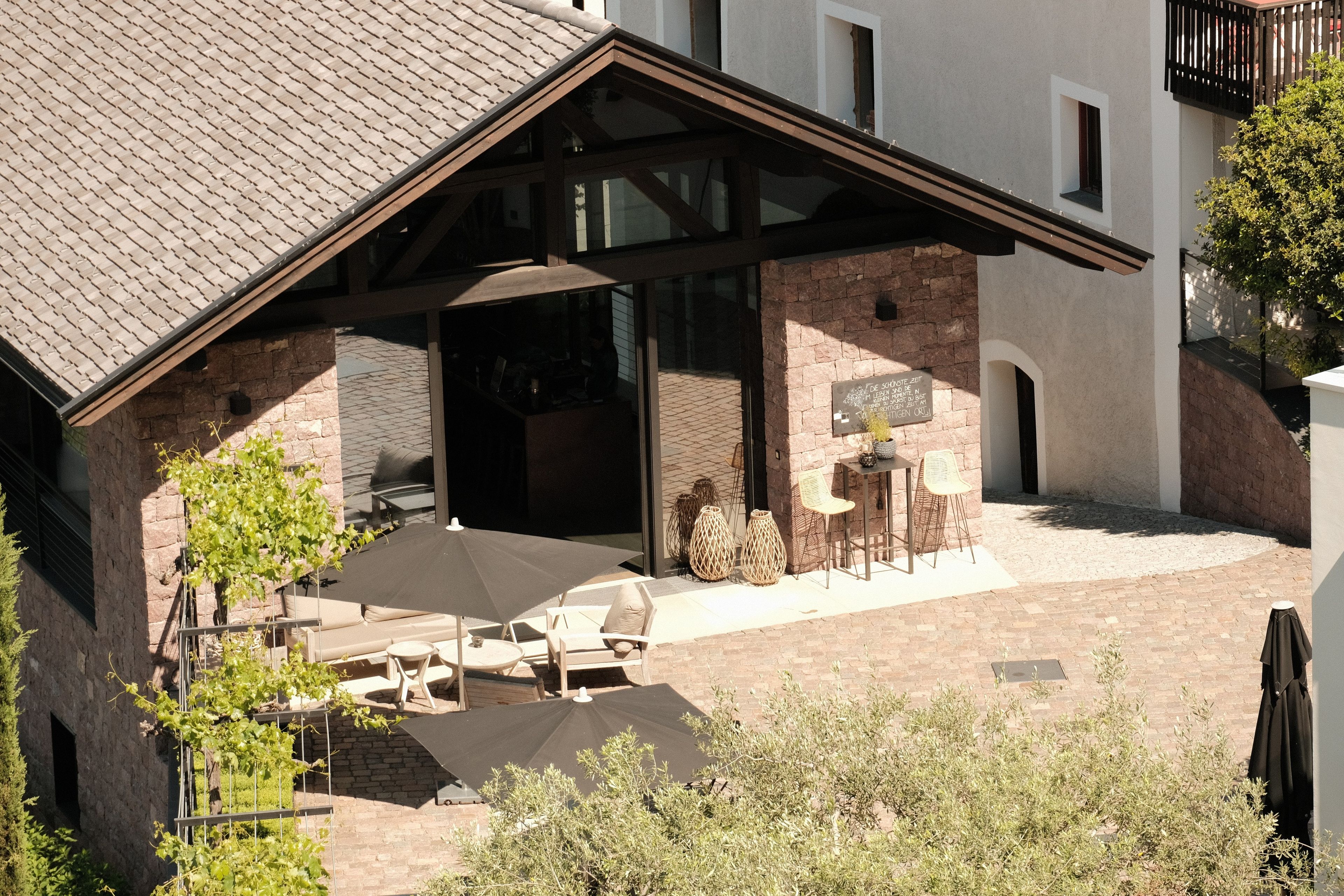 Un espace extérieur abrité, doté de tables et de chaises, une entrée avec une porte vitrée et une façade en briques.
