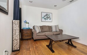 A living room with a sofa, a coffee table, a cabinet, and a wall-mounted artwork. - Cozy 1BR retreat with king bed, WiFi, fire pit, and walkable Fredericksburg charm. (Fredericksburg)