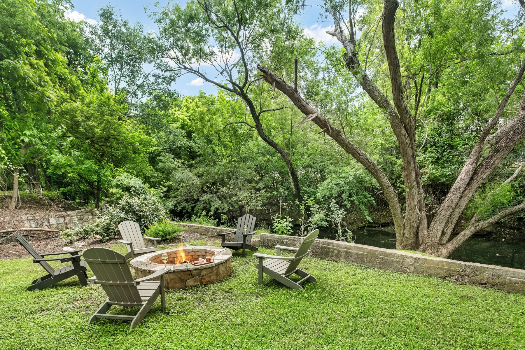 A fire pit surrounded by Adirondack chairs in a lush garden setting.