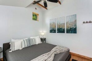 Een slaapkamer met een bed, nachtkastje, lamp, plafondventilator en een wandplank.