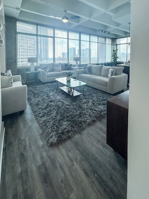 A modern living room with a large window, a glass coffee table, and a grey shag rug. - Altitude Apartments (Atlanta)