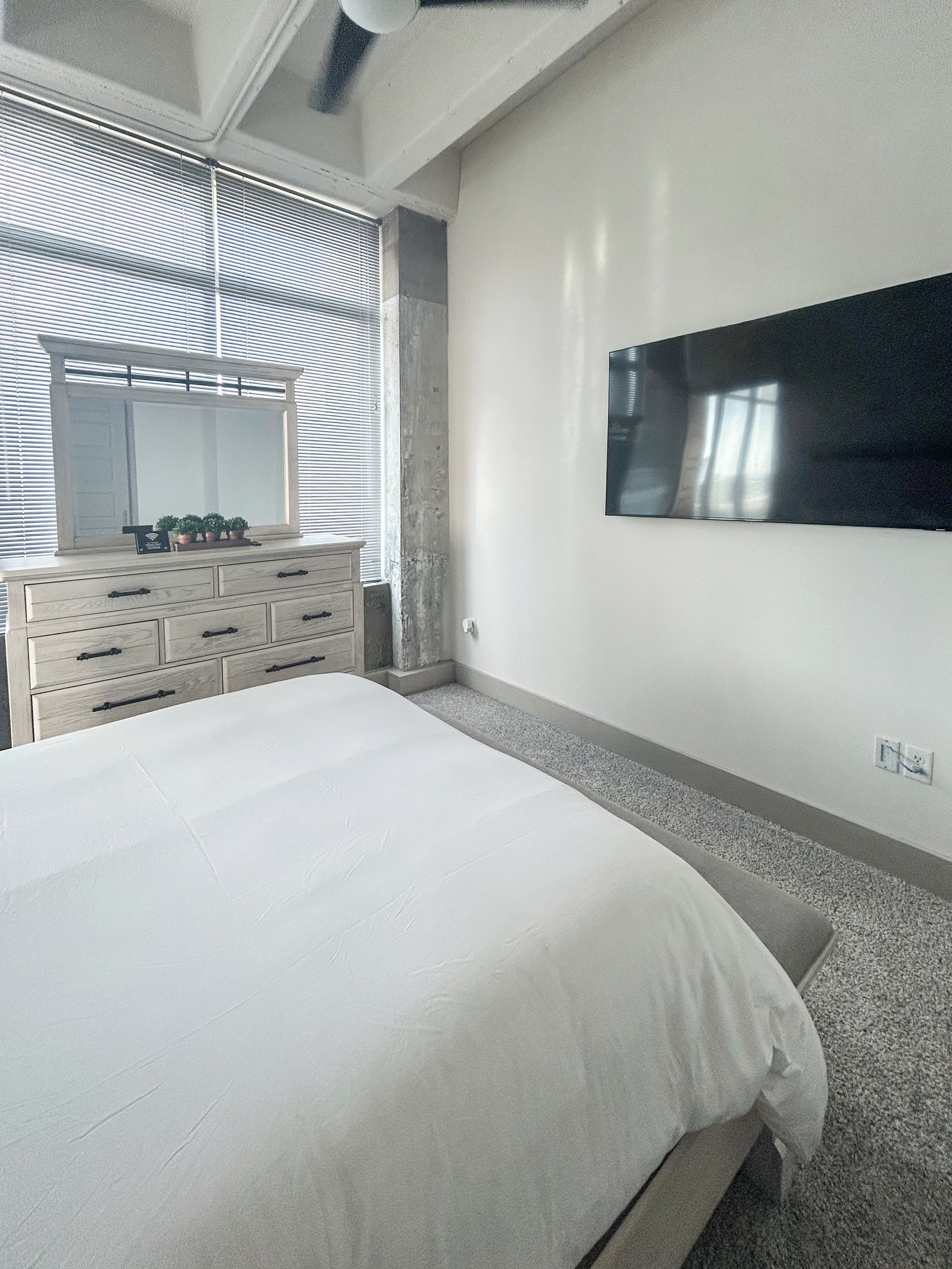 Un dormitorio con una cama grande, un aparador, un espejo y un televisor de pantalla plana montado en la pared.