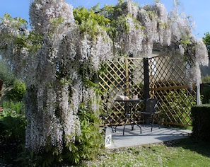 A garden with a pergola covered in white flowers, a table with chairs, and a small lantern. - Guest Room 'Entre Mer Et Terre - Chambre Rubis' with Shared Garden and Wi-Fi (Bazenville)