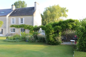 A two-story house with a well-maintained garden, a white fence, and a patio area with outdoor furniture.