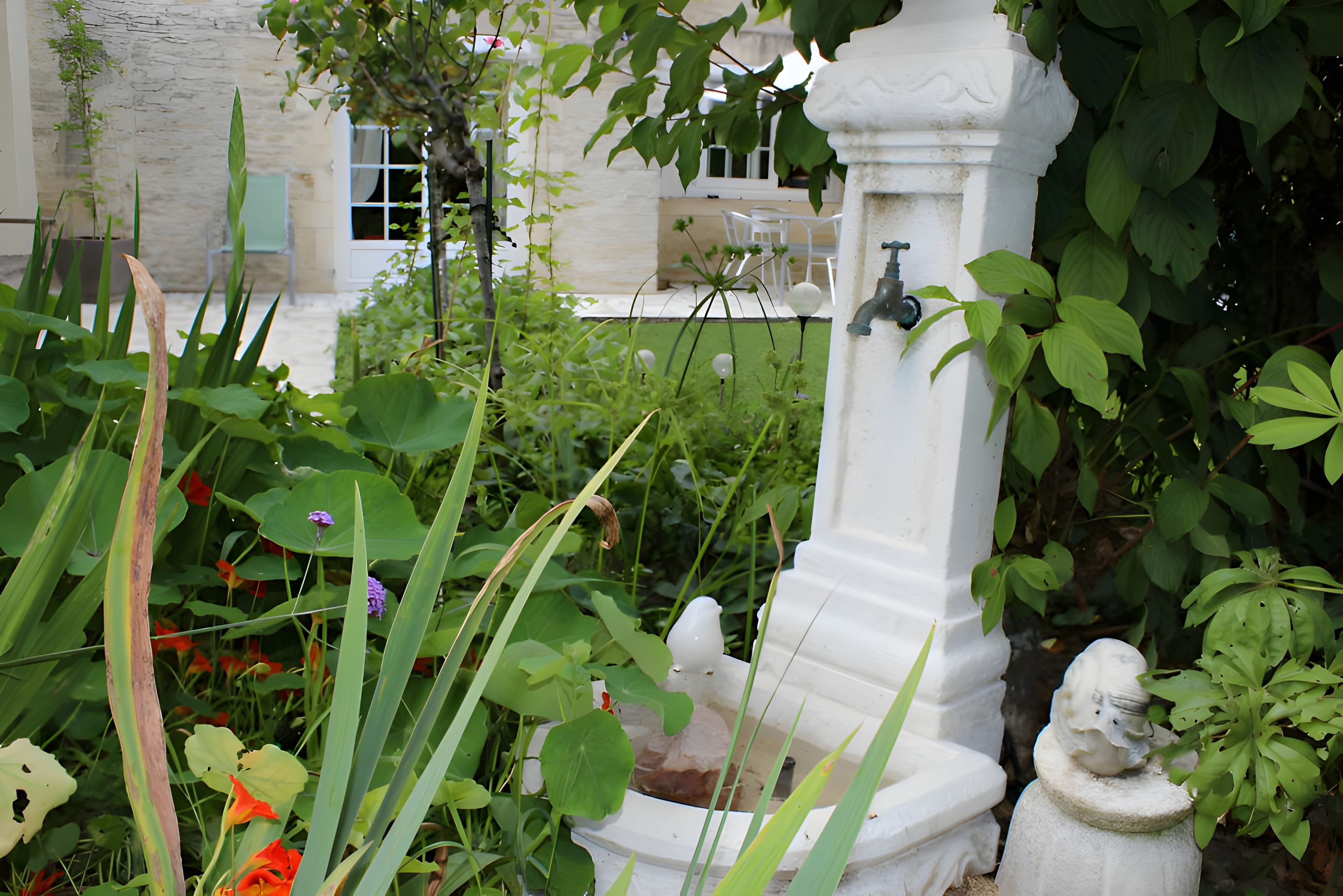 Ein Garten mit einer weißen Fontäne, einer Statue und üppigem Grün.