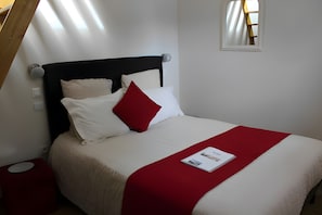 A neatly made bed with a red accent pillow, a white throw blanket, and a magazine on the bed.