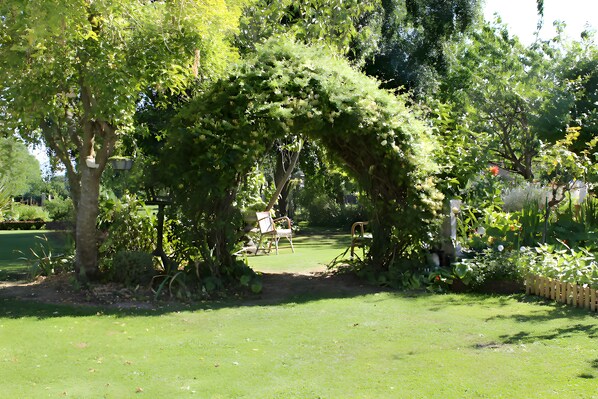 A garden with a central archway surrounded by lush greenery and a lawn.