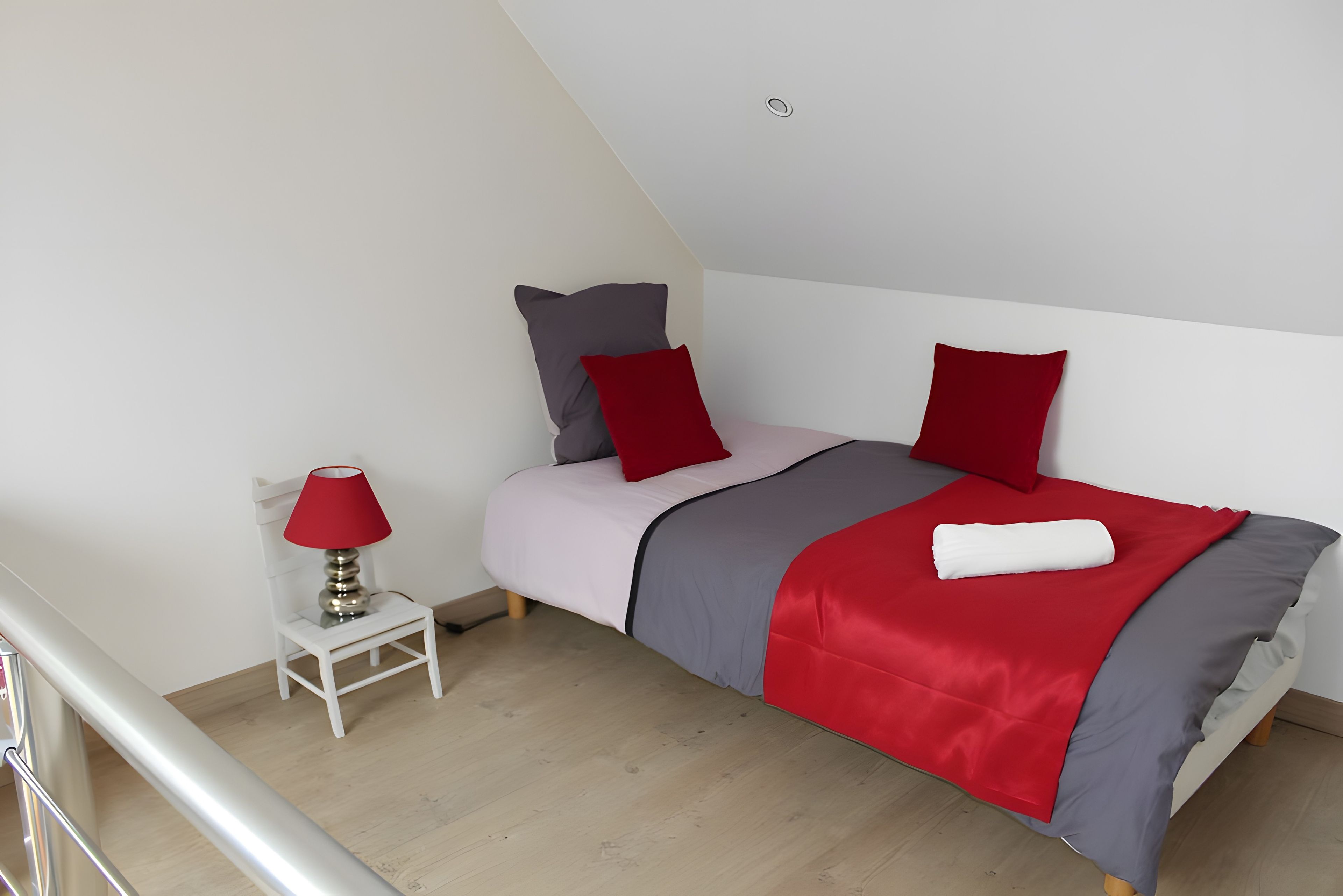 A bedroom with a bed, pillows, a red lamp, and a white chair.