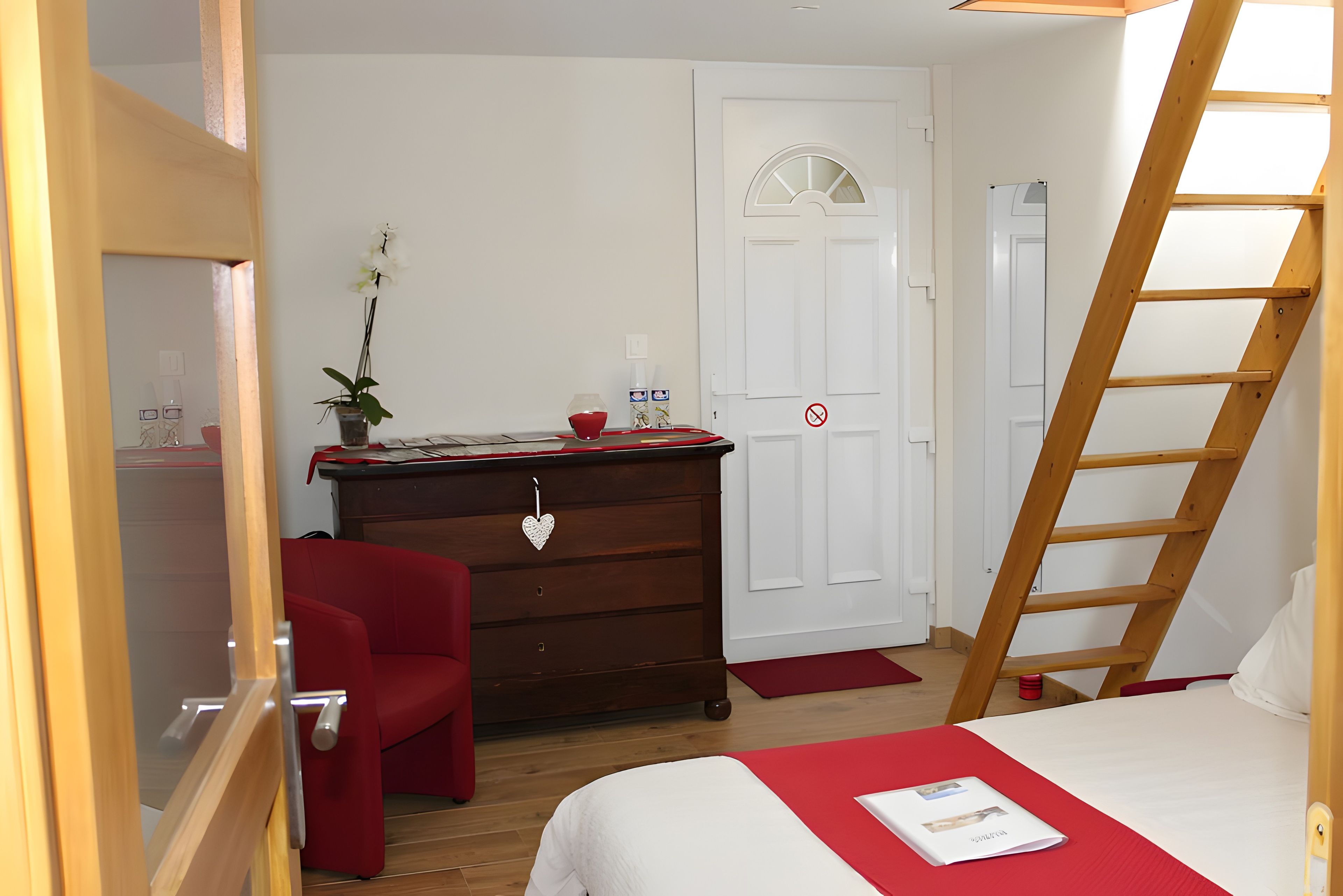 Een slaapkamer met een bed, een dressoir, een rode stoel, een bureau met een plant en een trap.
