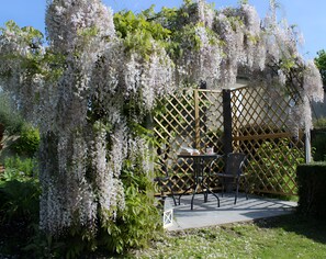 A garden with a pergola covered in white flowers, a table with chairs, and a small lantern. - Bed and Breakfast 'Entre Mer Et Terre - Chambre' with Shared Garden and Wi-Fi (Bazenville)