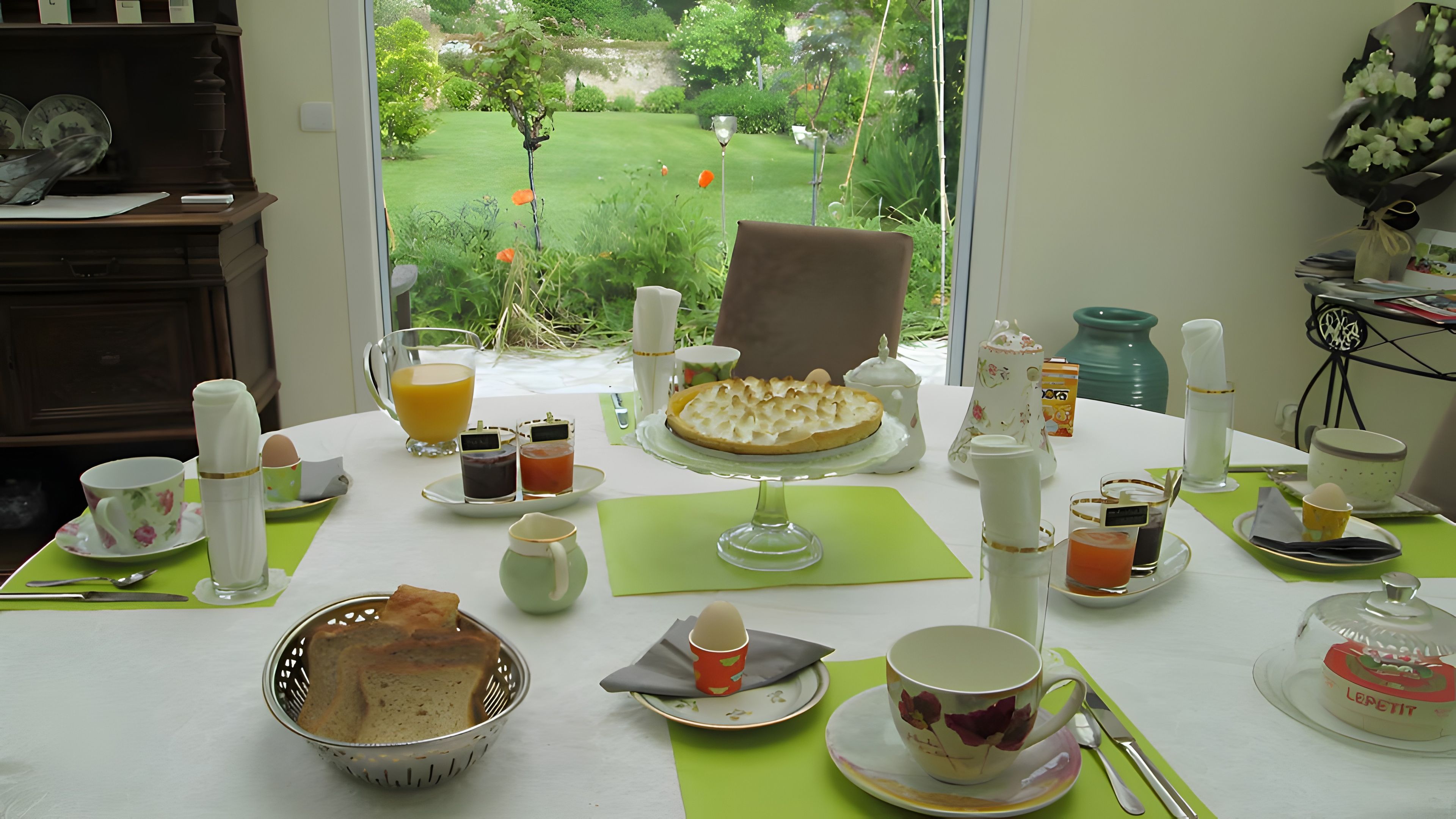 A breakfast table with a variety of items including a pie, beverages, and a basket of bread.