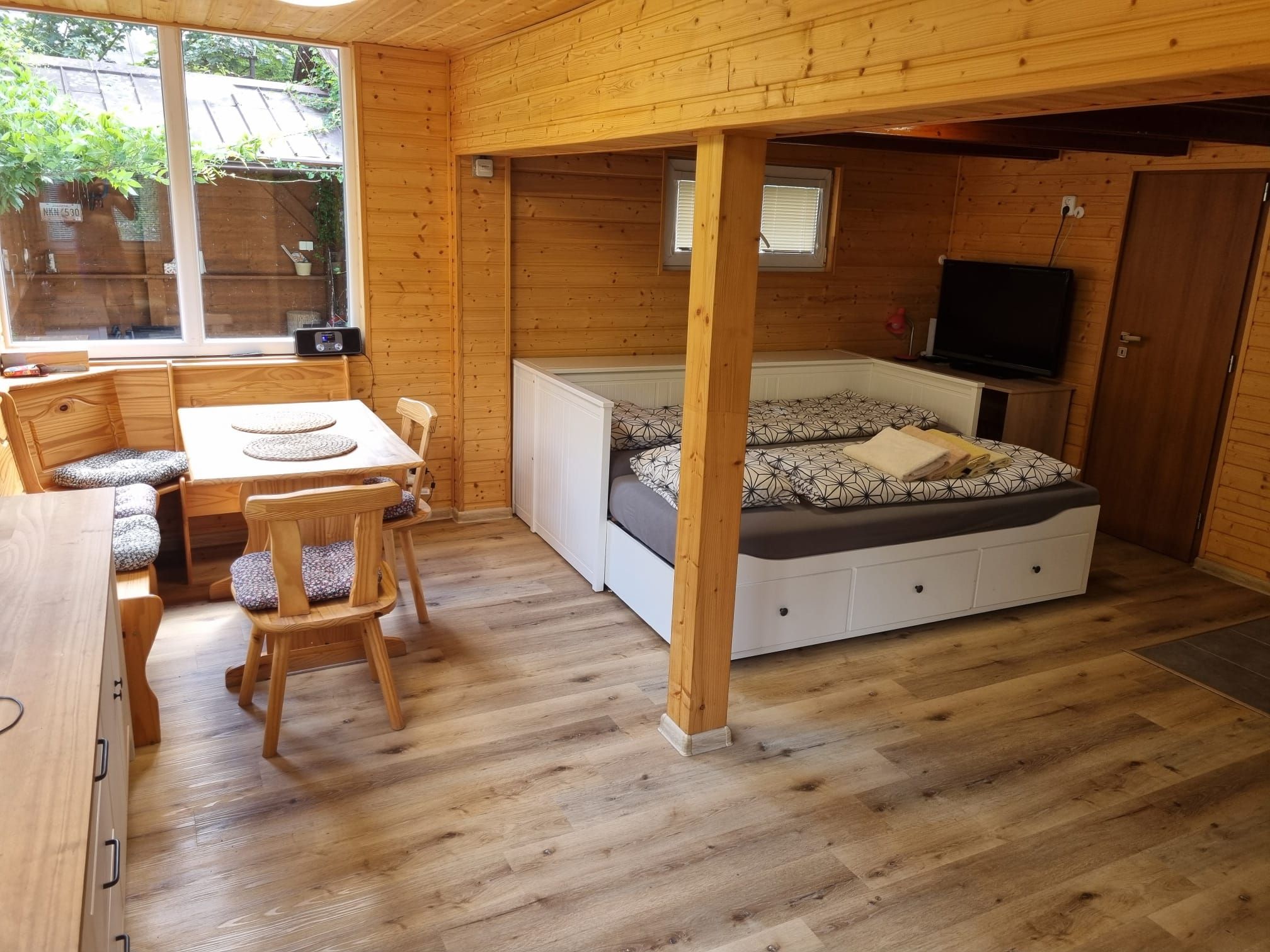 A wooden interior with a dining area, a bed with patterned bedding, and a television.