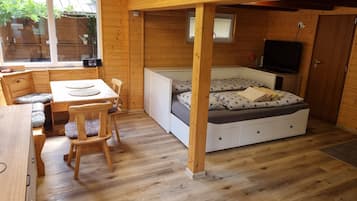 A wooden interior with a dining area, a bed with patterned bedding, and a television.