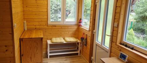 A wooden cabin interior with a bench, a small table, and a window with a view of greenery.